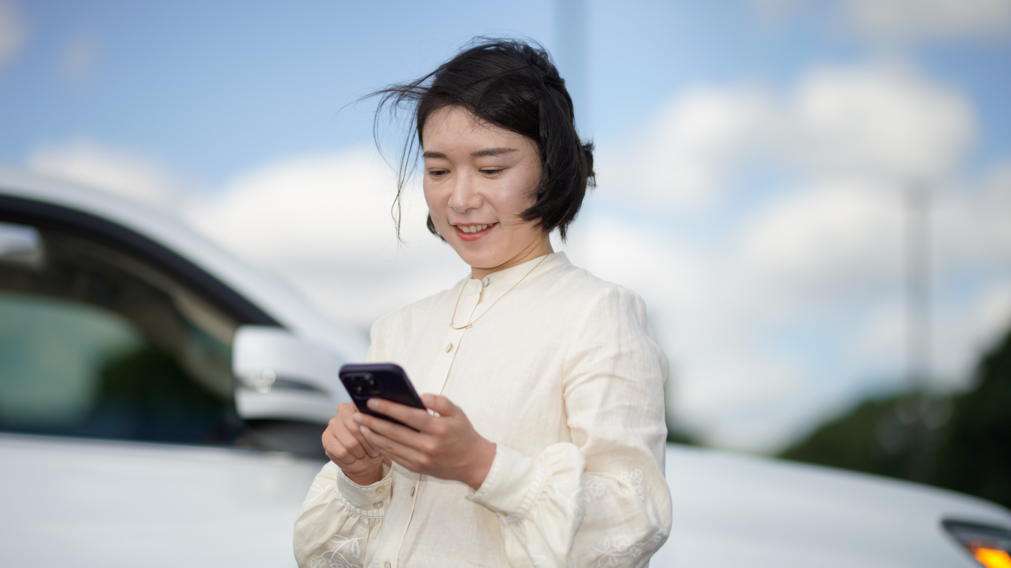 Buyer using phone to inspect under the hood of a car at a dealership